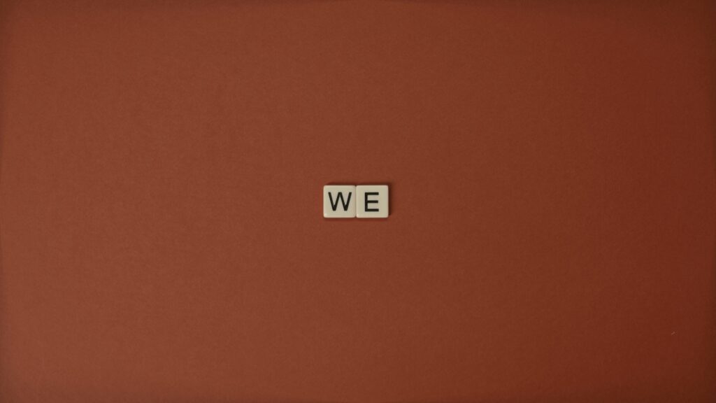 Close-up of Scrabble tiles spelling 'WE' on a brown background, symbolizing unity.